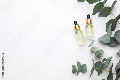 Bottles of eucalyptus essential oil and plant branches on white background  flat lay. Space for text