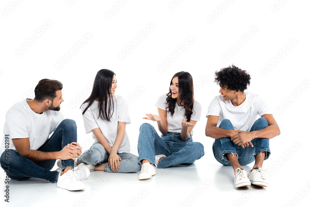 excited woman pointing with hands while talking to smiling interracial friends sitting on white. excited woman pointing with hands while talking to smiling interracial friends sitting on white.