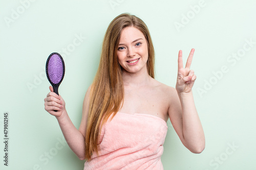 redhair woman smiling and looking friendly, showing number two. hair comb concept photo