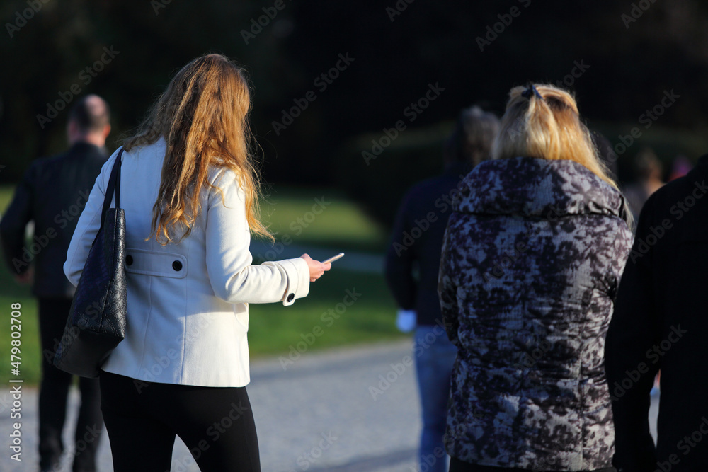Kobieta z telefonem w ręku spaceruje w parku z koleżanką. - obrazy, fototapety, plakaty 