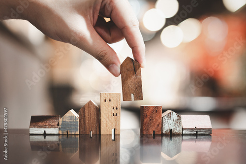 Hand choosing mini wood house model from model on wood table, selective focus, Planning to buy property. Choose what's the best. A symbol for construction ,ecology, loan concepts