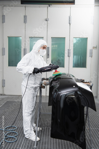 Workwoman in protective suit polishing car part in garage.