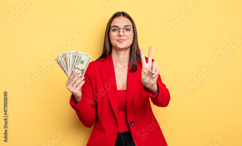 pretty woman smiling and looking friendly, showing number two. dollar banknotes concept photo