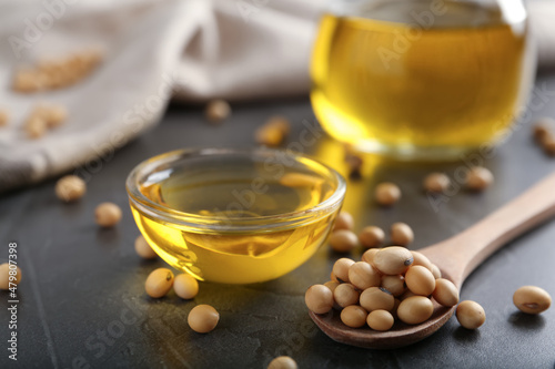 Bowl of oil and soybeans on grey table, closeup