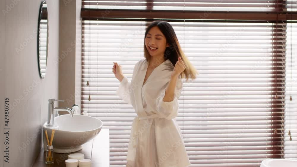 Cheerful Young Asian Female Wearing White Silk Robe Dancing In Bathroom Cheerful Young Asian Female Wearing White Silk Robe Dancing In Bathroom