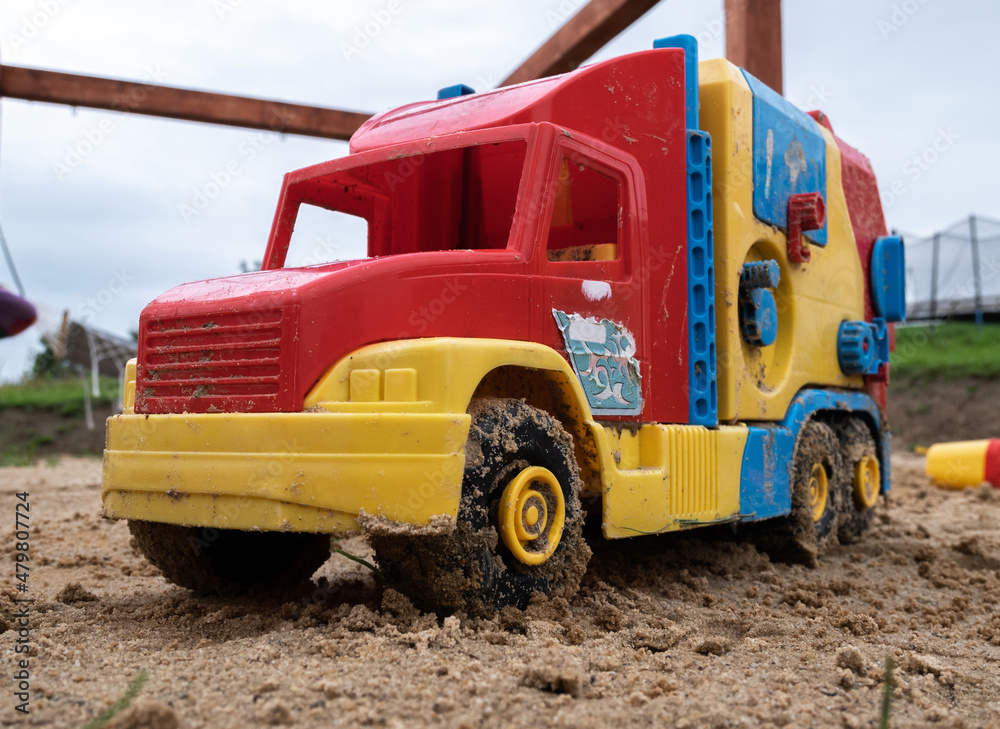Plastic toy garbage truck car in a sandbox on children playground in a public park.