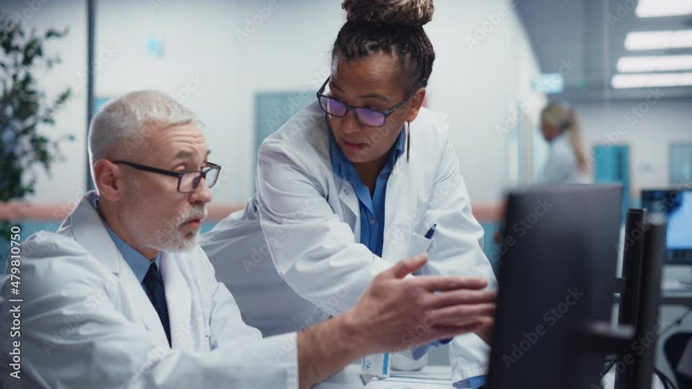 Medical Hospital: Two Doctors Talk and Use Computer, Doing Test Results Analysis. Health Care Clinic Research Laboratory: Black Female Chief Surgeon and White Male General Physicial Finding Cure Medical Hospital: Two Doctors Talk and Use Computer, Doing Test Results Analysis. Health Care Clinic Research Laboratory: Black Female Chief Surgeon and White Male General Physicial Finding Cure