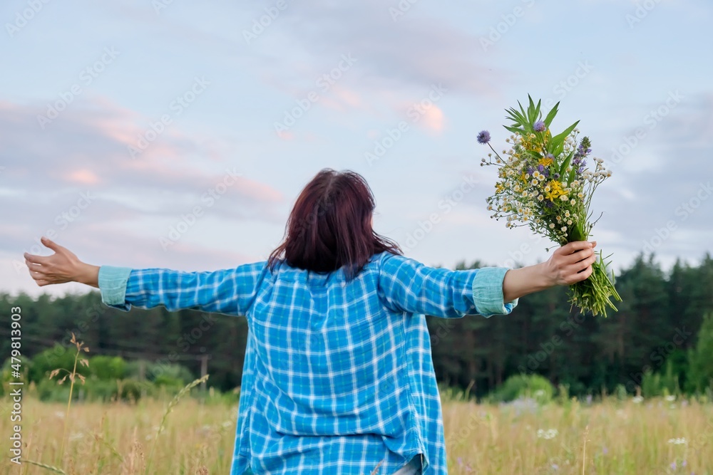 Woman with her back with raised arms with bouquet of wild flowers, summer nature Woman with her back with raised arms with bouquet of wild flowers, summer nature