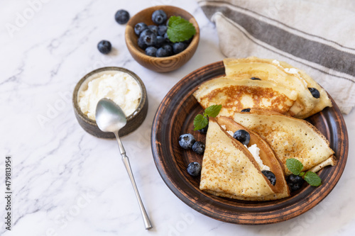Celebrating Pancake day, healthy breakfast. Delicious homemade crepes with blueberries and ricota on a stone tabletop. Copy space.