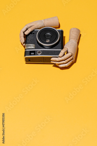Hands with instant camera on yellow studio background with copyspace