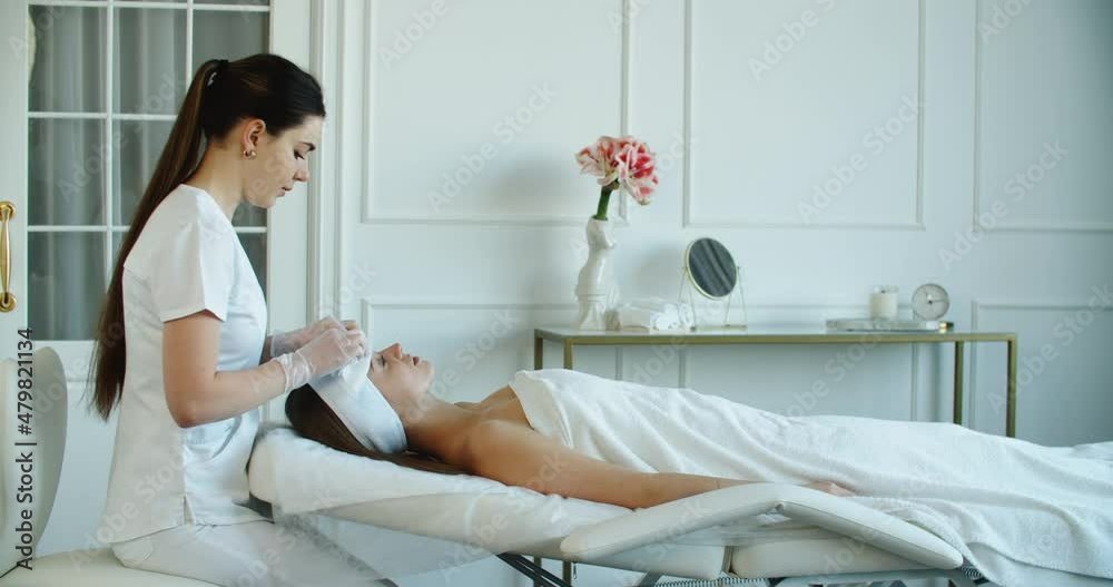 Curing skin problems. Female cosmetologist looking at client's face and giving a facial massage. Happy relaxed young woman getting professional facial treatment in spa salon. High quality 4k footage Curing skin problems. Female cosmetologist looking at client's face and giving a facial massage. Happy relaxed young woman getting professional facial treatment in spa salon. High quality 4k footage