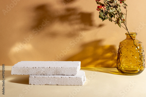 Background with geometric shapes made of concrete for cosmetic products. Rectangular podiums, glass vase with dried flowers and shadows on a beige background. Blank mockup for product