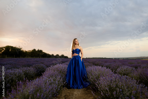 Young woman in a luxurious blue dress standing in a lavender field against the background of the sky.