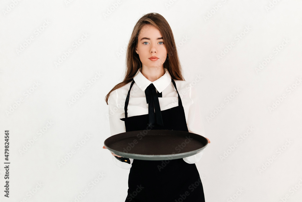 Portrait of a serious beautiful waitress with straight hair offering empty round black tray and looking at the camera isolated on white background Portrait of a serious beautiful waitress with straight hair offering empty round black tray and looking at the camera isolated on white background