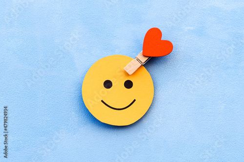 yellow happy smiley face on a blue background and a red heart as the emotion selection. The concept of mood selection and customer feedback. Copy space, business and emotions.