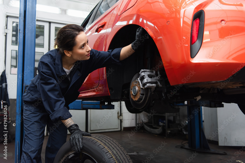 Workwoman in gloves checking car near tire in garage. Workwoman in gloves checking car near tire in garage.