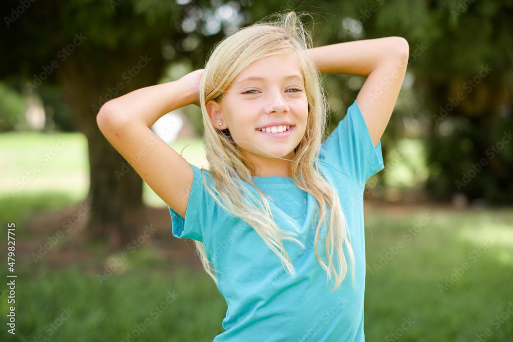 Caucasian little kid girl wearing blue T-shirt standing outdoors stretching arms, relaxed position. Caucasian little kid girl wearing blue T-shirt standing outdoors stretching arms, relaxed position.