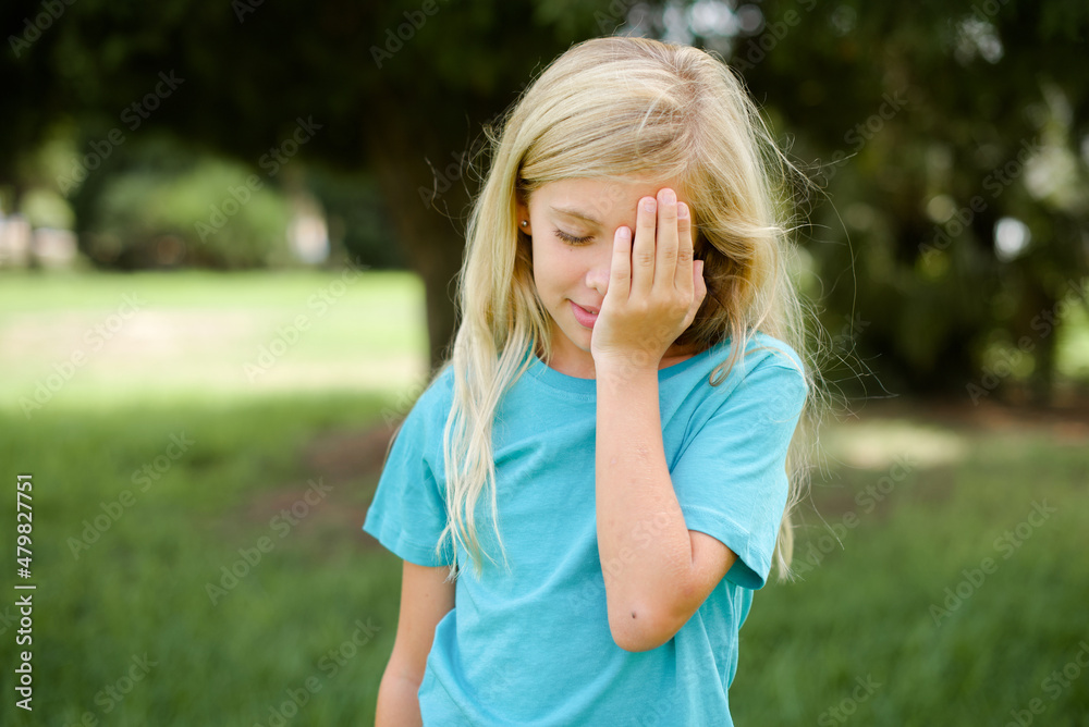 Tired overworked Caucasian little kid girl wearing blue T-shirt standing outdoors has sleepy expression, gloomy look, covers face with hand, has eyes shut, gasps from tiredness, fatigue after party Tired overworked Caucasian little kid girl wearing blue T-shirt standing outdoors has sleepy expression, gloomy look, covers face with hand, has eyes shut, gasps from tiredness, fatigue after party