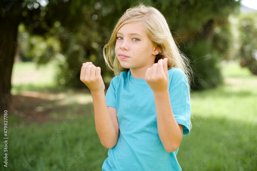 Caucasian little kid girl wearing blue T-shirt standing outdoors doing money gesture with hands, asking for salary payment, millionaire business Caucasian little kid girl wearing blue T-shirt standing outdoors doing money gesture with hands, asking for salary payment, millionaire business