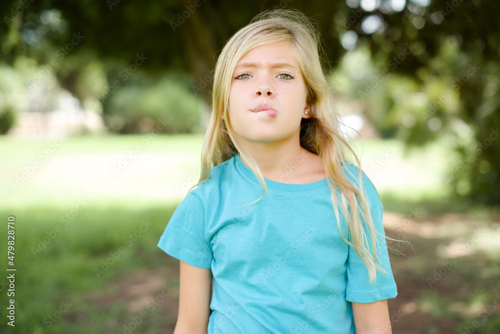 Caucasian little kid girl wearing blue T-shirt standing outdoors making grimace and crazy face, screaming out of control, funny lunatic expressing freedom and wild. Caucasian little kid girl wearing blue T-shirt standing outdoors making grimace and crazy face, screaming out of control, funny lunatic expressing freedom and wild.