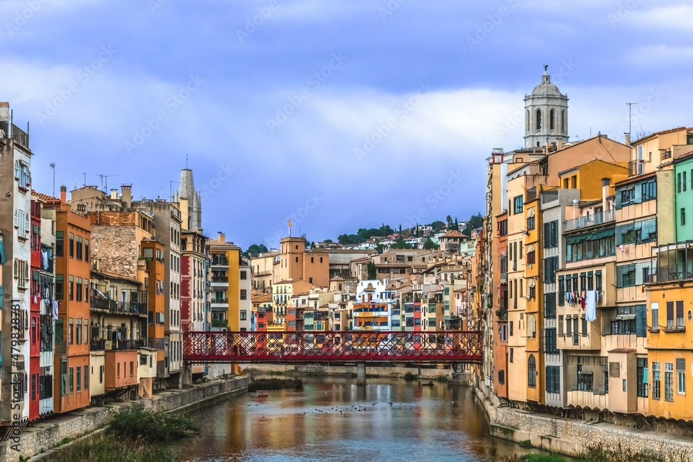 Girona cityscape with Eiffel bridge over Onyar river, Spain. Urban panorama with bright colorful old buildings on the sides of a water stream