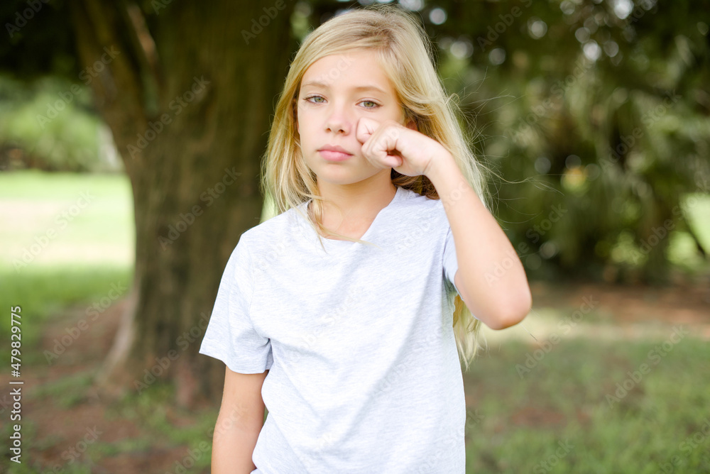 Disappointed dejected Caucasian little kid girl wearing whiteT-shirt standing outdoors wipes tears stands stressed with gloomy expression. Negative emotion Disappointed dejected Caucasian little kid girl wearing whiteT-shirt standing outdoors wipes tears stands stressed with gloomy expression. Negative emotion