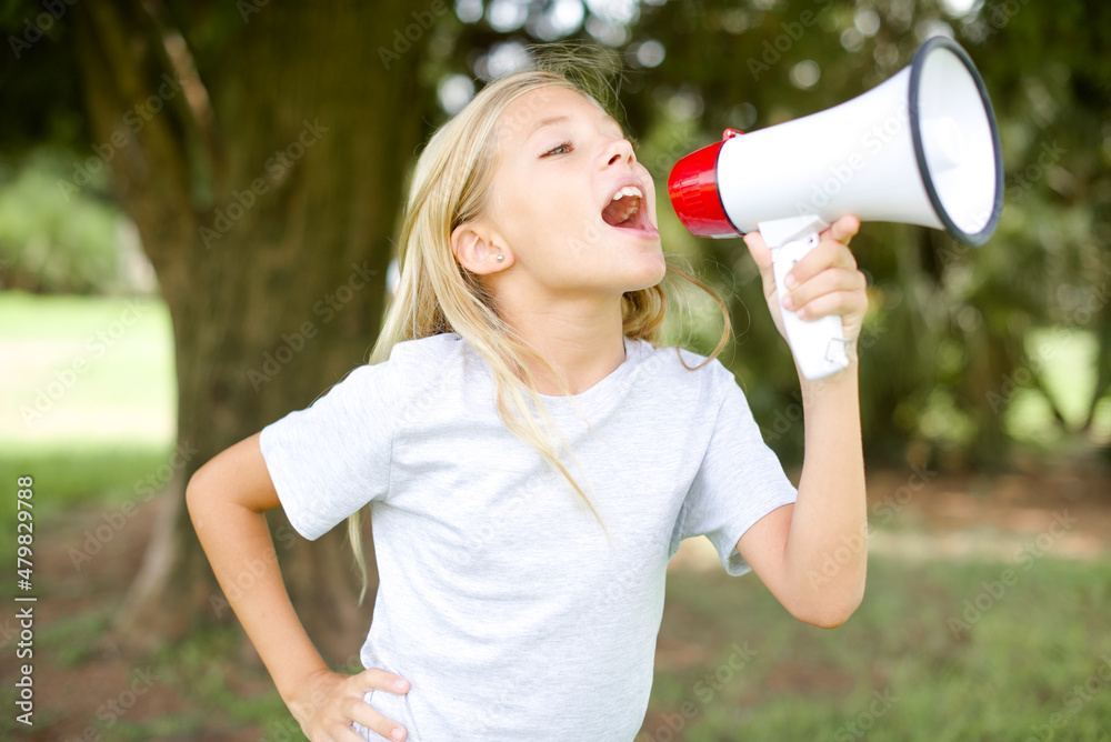 Funny Caucasian little kid girl wearing whiteT-shirt standing outdoors People sincere emotions lifestyle concept. Mock up copy space. Screaming in megaphone. Funny Caucasian little kid girl wearing whiteT-shirt standing outdoors People sincere emotions lifestyle concept. Mock up copy space. Screaming in megaphone.