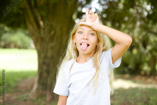 Canvas Print Caucasian little kid girl wearing whiteT-shirt standing outdoors gestures with f