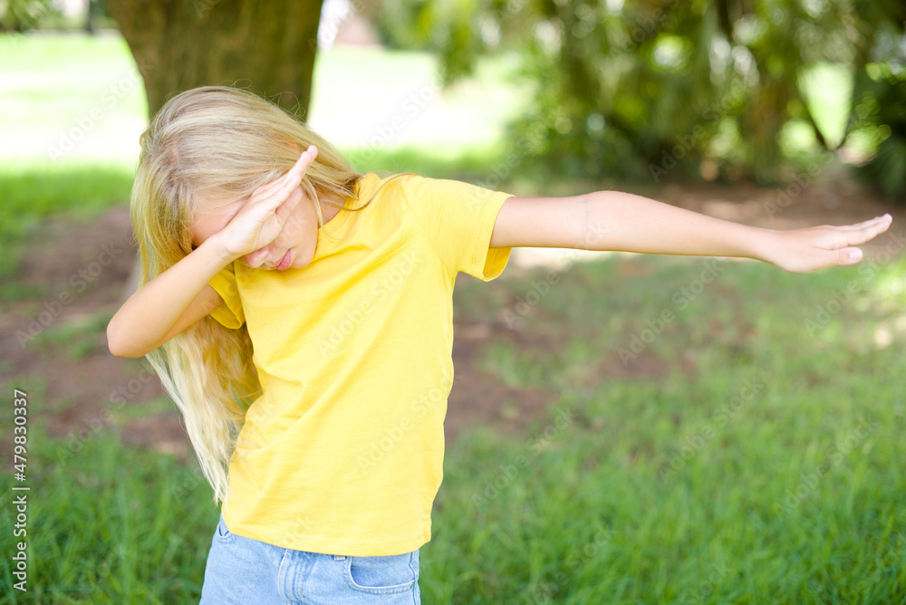 Photo of funky beautiful Caucasian little kid girl wearing yellow T-shirt standing outdoors show disco move dab