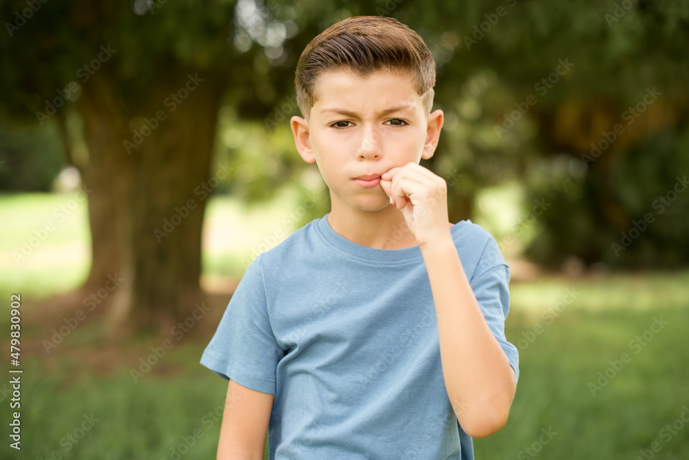 beautiful Caucasian little kid boy wearing blue T-shirt standing outdoors mouth and lips shut as zip with fingers. Secret and silent, taboo talking. beautiful Caucasian little kid boy wearing blue T-shirt standing outdoors mouth and lips shut as zip with fingers. Secret and silent, taboo talking.