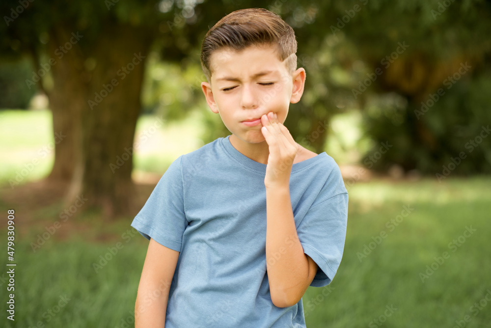 beautiful Caucasian little kid boy wearing blue T-shirt standing outdoors touching mouth with hand with painful expression because of toothache or dental illness on teeth. beautiful Caucasian little kid boy wearing blue T-shirt standing outdoors touching mouth with hand with painful expression because of toothache or dental illness on teeth.