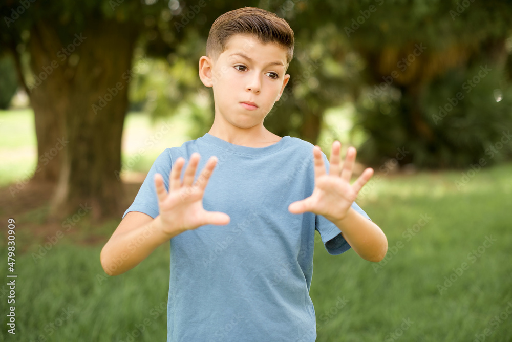 beautiful Caucasian little kid boy wearing blue T-shirt standing outdoors Moving away hands palms showing refusal and denial with afraid and disgusting expression. Stop and forbidden. beautiful Caucasian little kid boy wearing blue T-shirt standing outdoors Moving away hands palms showing refusal and denial with afraid and disgusting expression. Stop and forbidden.