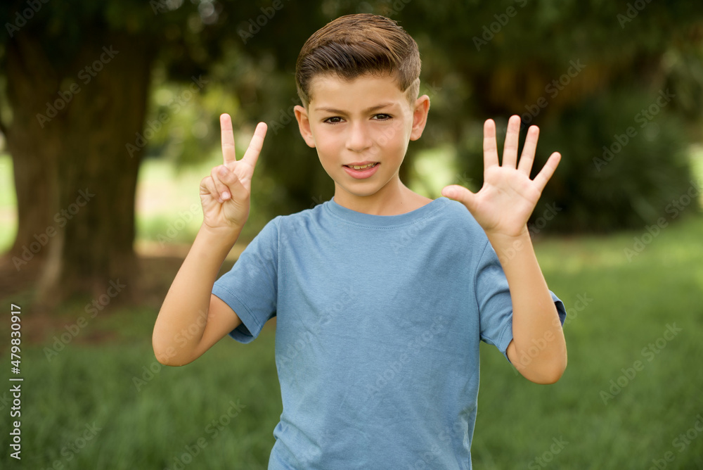 beautiful Caucasian little kid boy wearing blue T-shirt standing outdoors showing and pointing up with fingers number seven while smiling confident and happy. beautiful Caucasian little kid boy wearing blue T-shirt standing outdoors showing and pointing up with fingers number seven while smiling confident and happy.
