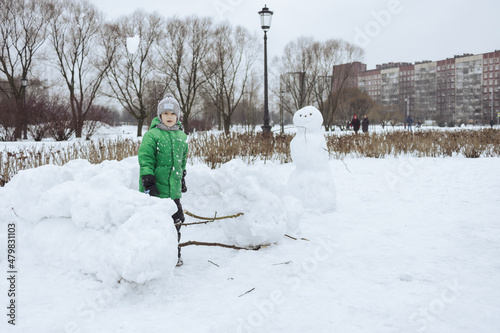 Happy boy standing inside snowcastle and play snowball game in winter park photo