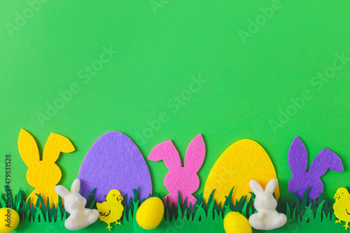 Colorful Easter bunnies, eggs and chickens in grass on green background, top view with space for text. Happy Easter! Pink and yellow artificial eggs and bunnies decor with green grass