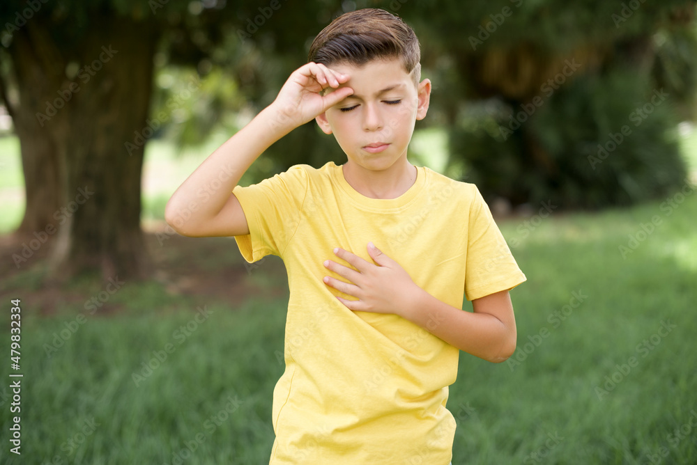 Caucasian little kid boy wearing yellow T-shirt standing outdoor Touching forehead for illness and fever, flu and cold, virus sick. Caucasian little kid boy wearing yellow T-shirt standing outdoor Touching forehead for illness and fever, flu and cold, virus sick.