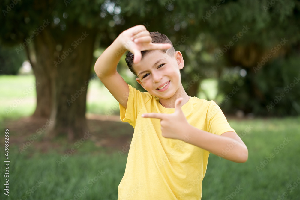 Caucasian little kid boy wearing yellow T-shirt standing outdoor making finger frame with hands. Creativity and photography concept. Caucasian little kid boy wearing yellow T-shirt standing outdoor making finger frame with hands. Creativity and photography concept.