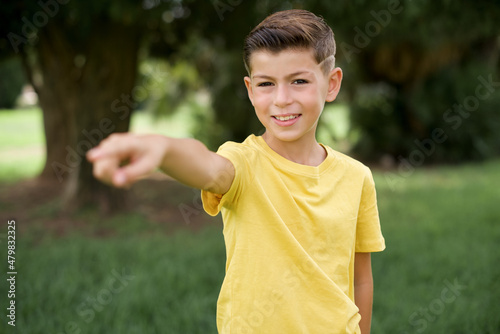 Caucasian little kid boy wearing yellow T-shirt standing outdoor pointing displeased and frustrated to the camera, angry and furious ready to fight with you.