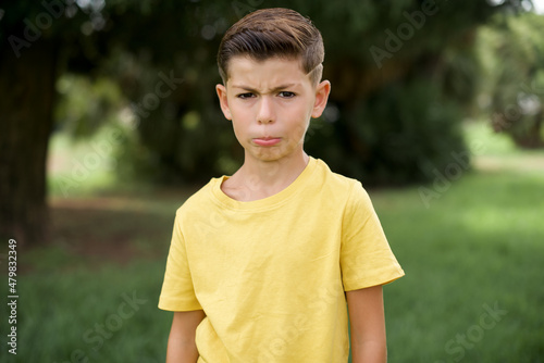 Displeased upset Caucasian little kid boy wearing yellow T-shirt standing outdoor  frowns face as going to cry, being discontent and unhappy as can't achieve goals,  Disappointed model has troubles © Roquillo