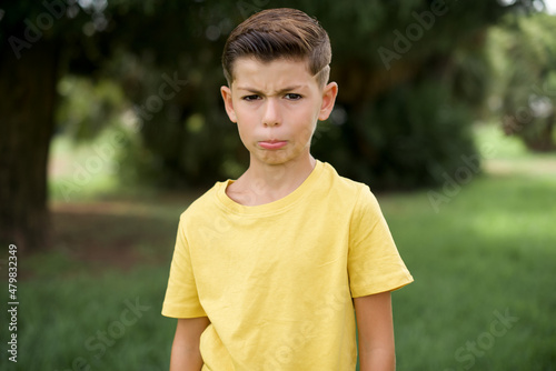 Displeased upset Caucasian little kid boy wearing yellow T-shirt standing outdoor frowns face as going to cry, being discontent and unhappy as can't achieve goals, Disappointed model has troubles