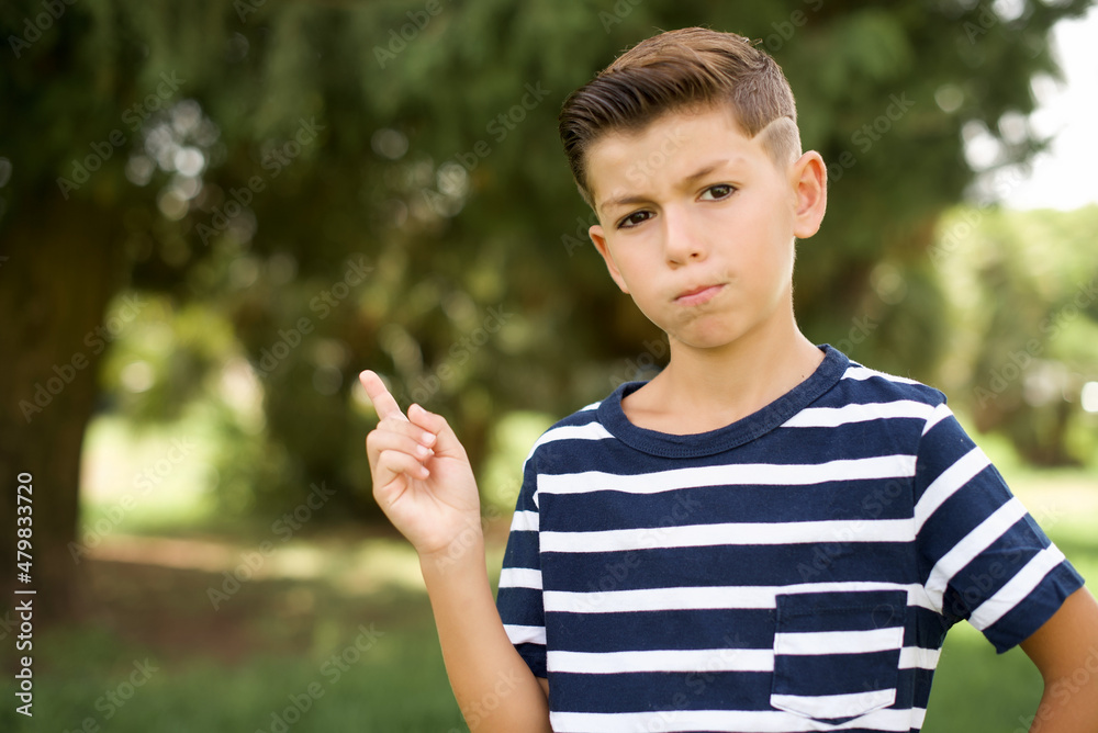 beautiful Caucasian little kid boy wearing stripped T-shirt standing outdoors points to side on blank space demonstrates advertisement. People and promotion concept beautiful Caucasian little kid boy wearing stripped T-shirt standing outdoors points to side on blank space demonstrates advertisement. People and promotion concept