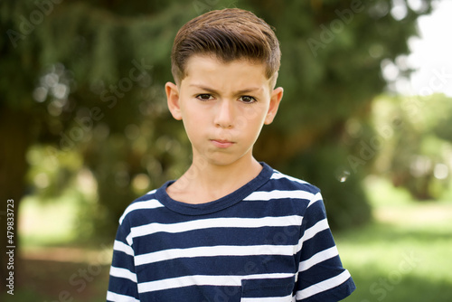 beautiful Caucasian little kid boy wearing stripped T-shirt standing outdoors Pointing down with fingers showing advertisement, surprised face and open mouth