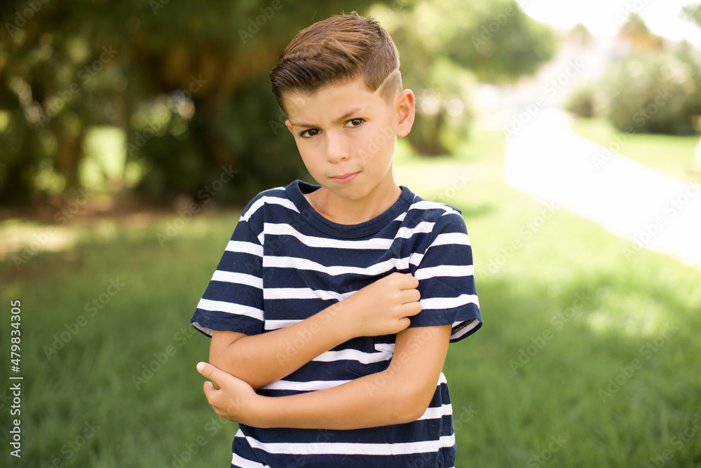 Confident beautiful Caucasian little kid boy wearing stripped T-shirt standing outdoors with arms crossed looking to the camera Confident beautiful Caucasian little kid boy wearing stripped T-shirt standing outdoors with arms crossed looking to the camera