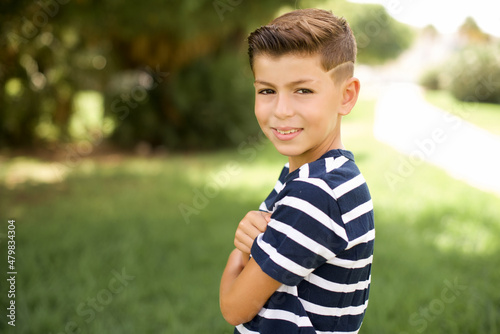 Portrait of beautiful Caucasian little kid boy wearing stripped T-shirt standing outdoors standing with folded arms and smiling