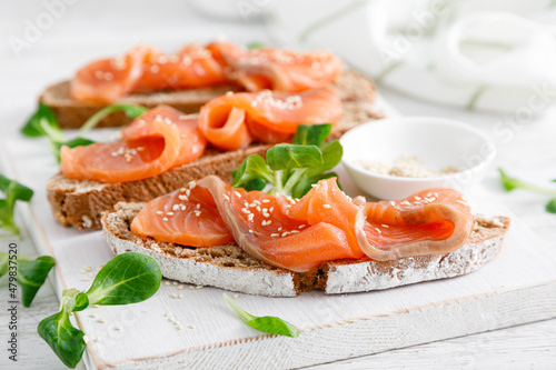 Whole grain rye bread open sandwiches with salted salmon on a white rustic wooden table. Healthy food photo