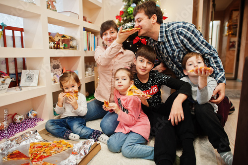 Happy family with four kids eating pizza at home.