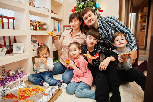 Happy family with four kids eating pizza at home.