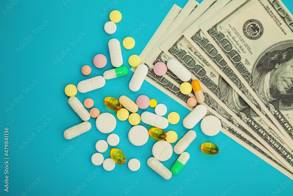 Money pills. Medicine pills on dollar bills on a blue background Covid-19 coronavirus pills are in one hundred dollar bills. The concept of insurance medicine, insurance, high cost high cost of drugs. Money pills. Medicine pills on dollar bills on a blue background Covid-19 coronavirus pills are in one hundred dollar bills. The concept of insurance medicine, insurance, high cost high cost of drugs.