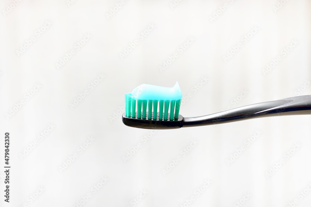 black toothbrush with toothpaste applied to it on a light background black toothbrush with toothpaste applied to it on a light background