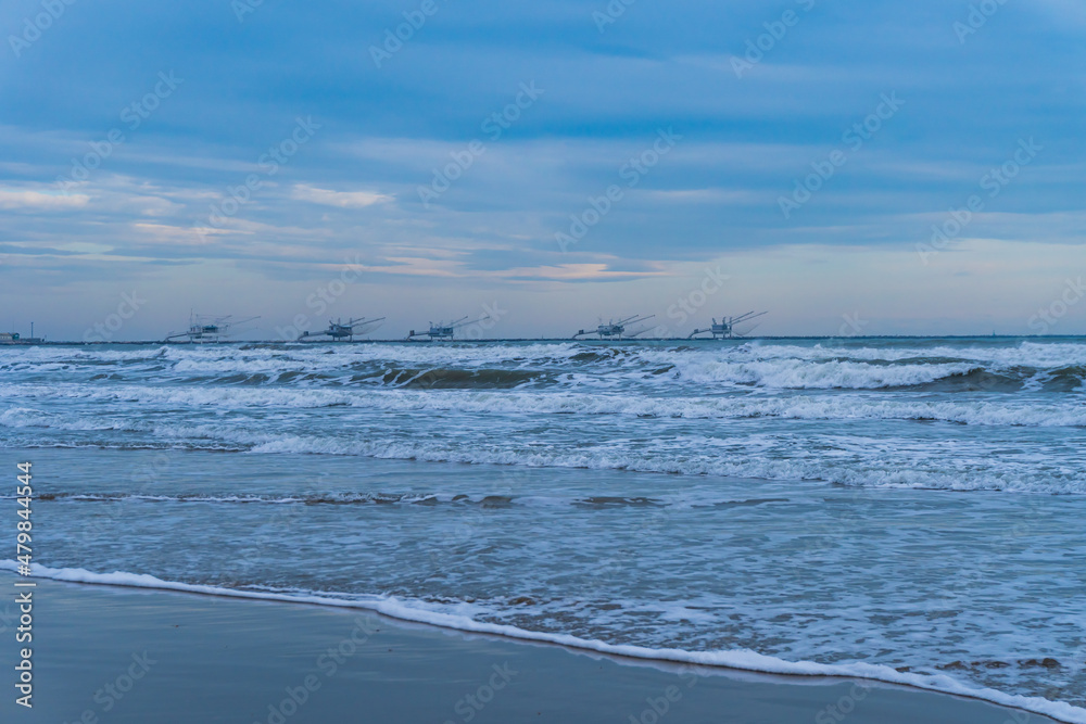 Scena con il mare con le onde e la spiaggia e dei padelloni sullo sfondo a Marina di Ravenna, in Italia, in inverno. Viaggiare. Vacanze. Destinazione. Paesaggio marino. Scena con il mare con le onde e la spiaggia e dei padelloni sullo sfondo a Marina di Ravenna, in Italia, in inverno. Viaggiare. Vacanze. Destinazione. Paesaggio marino.